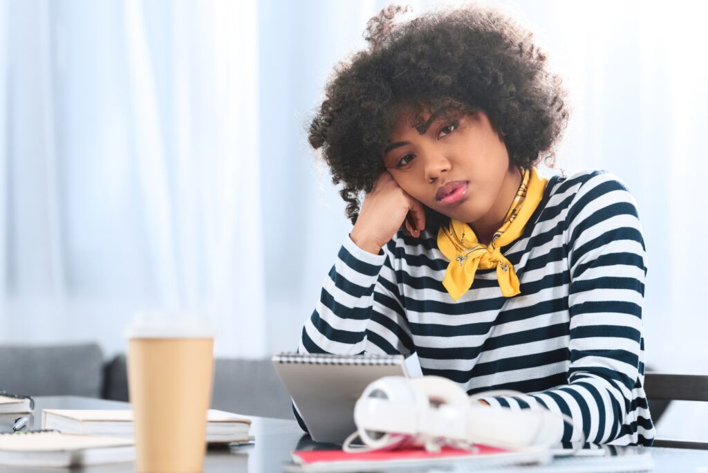 portrait of bored african american student with notebook sitting at table