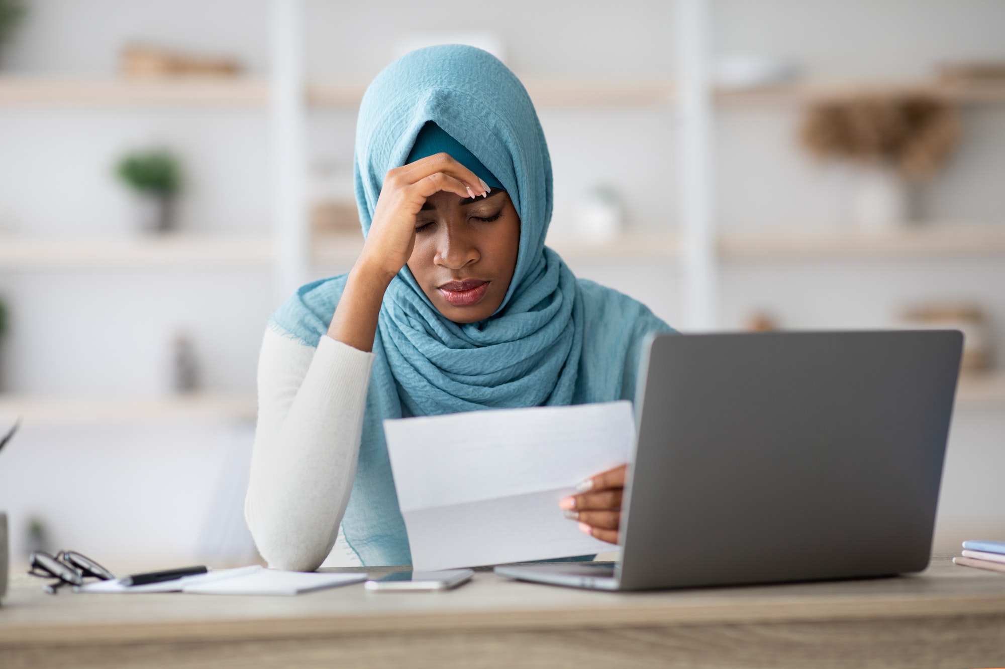 Stressed Black Muslim Woman Working With Papers And Laptop In Office