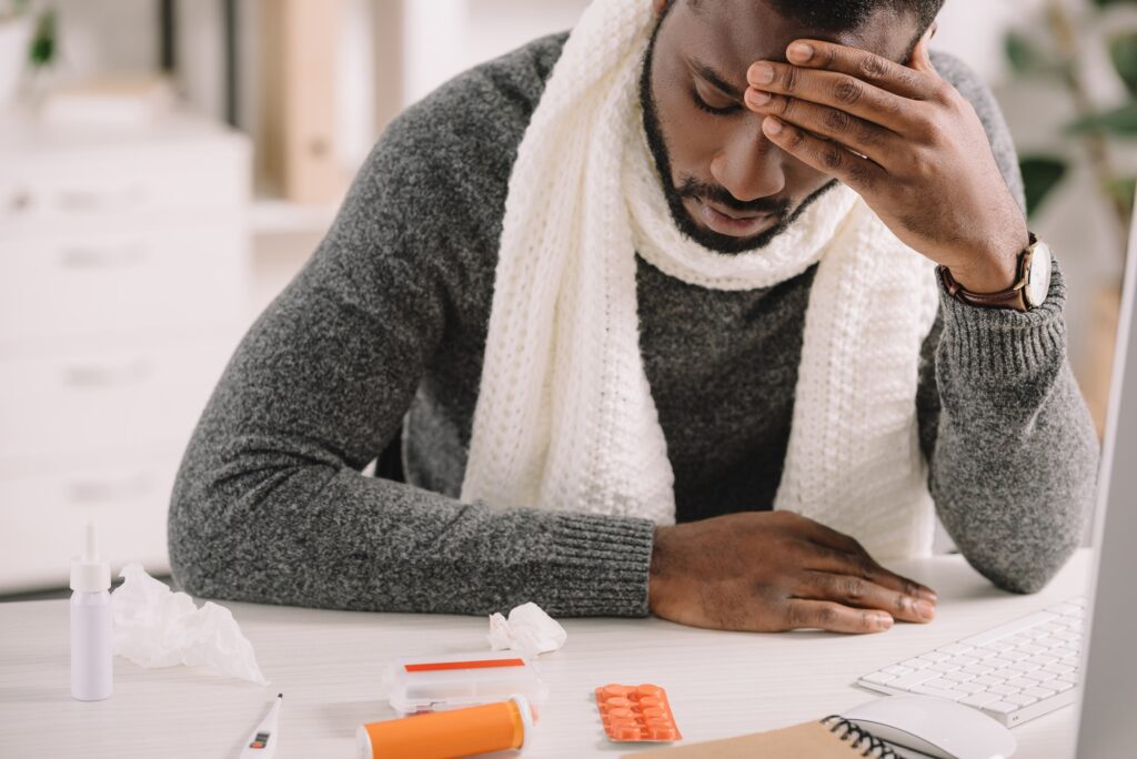 tired african american man with headache looking at pills while sitting in office